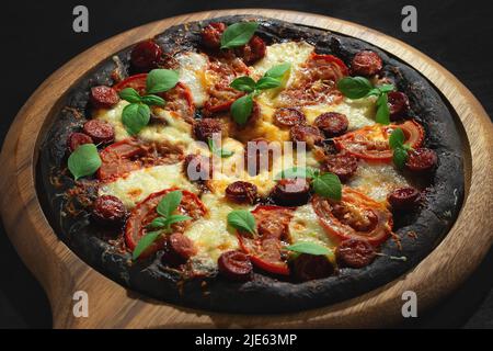 Pizza noire avec tomates, saucisses, mozzarella et basilic.Pâte à base de poudre de charbon de bambou saine. Banque D'Images
