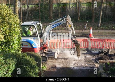 Workman utilise une minipelle pour creuser une chaussée (trottoir) par une route dans une zone résidentielle Banque D'Images