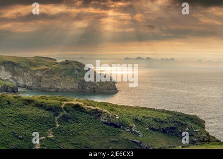 La mer scintille tandis que le soleil traverse les nuages sur le sentier côtier et la vallée des Rocheuses à Tarthevy, près de Tintagel, dans la Cornouailles du Nord. Banque D'Images