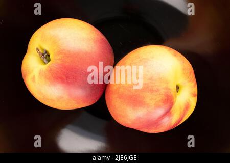 Deux nectarines mûres juteuses sur une plaque en céramique noire, vue rapprochée, vue de dessus. Banque D'Images