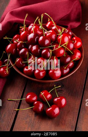 Cerises rouges fraîches dans une assiette en argile sur une serviette rouge. Cerises mûres sur des planches de bois. Concept alimentaire sain. Gros plan Banque D'Images