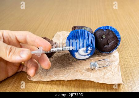 Homme avec une seringue injectant de l'insuline dans la vue de côté de muffin chocolat moulant. Banque D'Images