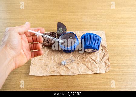 Homme avec une seringue injectant de l'insuline dans un muffin au chocolat moulant. Banque D'Images