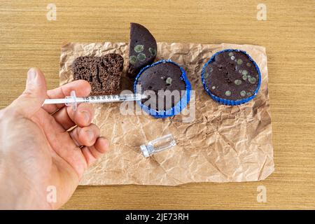 Homme avec une seringue injectant de l'insuline dans un muffin au chocolat moulant vue de dessus. Banque D'Images