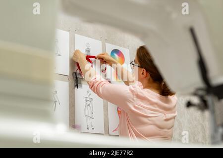 Le designer de mode développe des croquis de la conception de vêtements. L'artiste crée des robes pour femmes. Travailler sur mesure avec le tissu. Banque D'Images