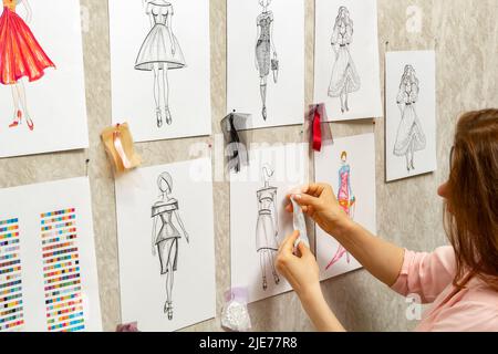 Le designer de mode développe des croquis de la conception de vêtements. L'artiste crée des robes pour femmes. Travailler sur mesure avec le tissu. Banque D'Images