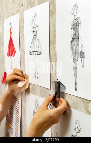 Le designer de mode développe des croquis de la conception de vêtements. L'artiste crée des robes pour femmes. Travailler sur mesure avec le tissu. Banque D'Images