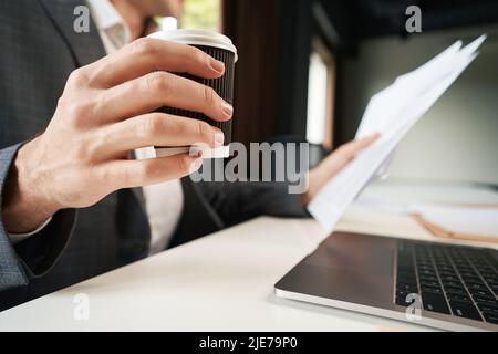 Un employé soulève une tasse à café tout en travaillant avec la documentation Banque D'Images