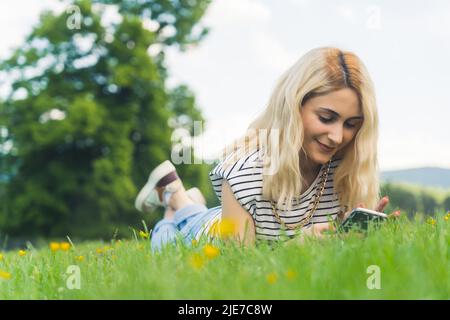 Blonde caucasienne fille couché sur l'herbe et à l'aide d'un téléphone portable. Plein air. Photo de haute qualité Banque D'Images