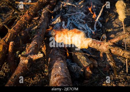 Bâton de pain cuit sur feu de camp. Pâte à pain tordue sur bâton de bois et torréfiée au feu. Nourriture de camping amusante pour les enfants. Barbecue ou barbecue à la plage. Banque D'Images