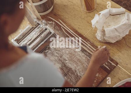 Tranchez des nouilles faites maison sur un trancheuse à nouilles sur un panneau de bois de cuisine et un sac de farine Banque D'Images