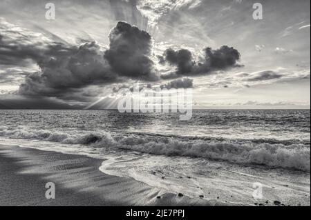 Les rayons du soleil éclatants traversent les nuages dans un paysage de coucher de soleil sur l'océan noir et blanc Banque D'Images