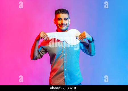 Portrait d'homme positif en chemise tenant une énorme clé en papier et souriant satisfait de la nouvelle maison, l'achat immobilier, le service de location. Studio d'intérieur isolé sur fond de néon coloré. Banque D'Images