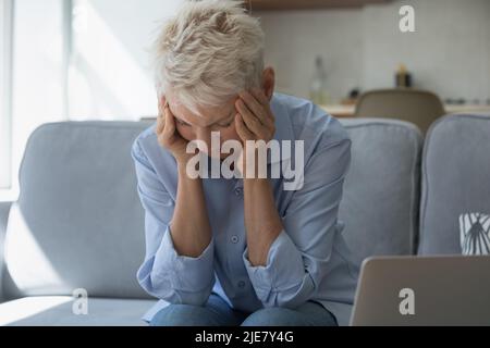 Contrarié la femme âgée tenant la tête avec les mains assis sur le canapé Banque D'Images