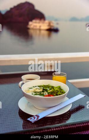 Tôt le matin, petit-déjeuner composé de jus d'orange, café et un bol de soupe aux nouilles poulet et ric à bord d'un navire de croisière de luxe sur la baie d'Halong Banque D'Images