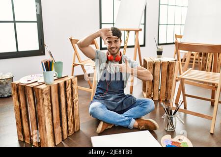 Jeune homme hispanique assis dans un studio d'art souriant faisant cadre avec les mains et les doigts avec le visage heureux. Créativité et concept de photographie. Banque D'Images