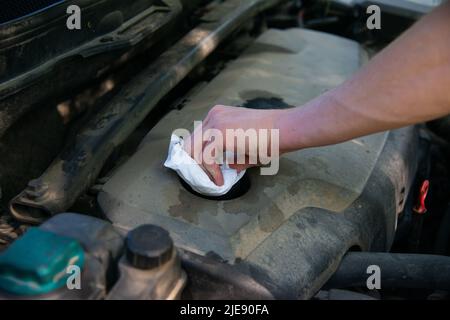 La main de l'homme dévisse le bouchon de la goulotte de remplissage d'huile du moteur. Des gants de mécanicien changent l'huile moteur, puis le moteur est en service. Banque D'Images