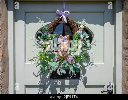 Guirlande charmante avec écureuil de paille entourée de graminées et de fleurs accrochées à la porte d'entrée rustique Banque D'Images