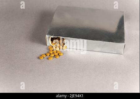 Une boîte rectangulaire argentée sur fond gris. La nourriture pour animaux déborde du trou. Aliments secs en pellicule. Nourriture pour animaux. Mise au point sélective. Banque D'Images