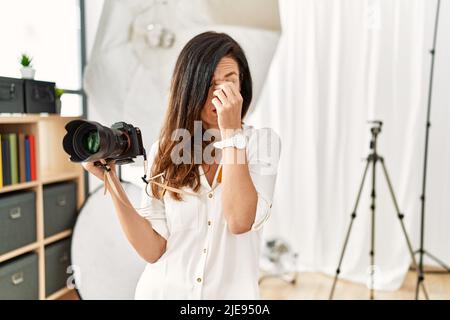 Belle femme caucasienne travaillant comme photographe au studio de photographie fatigué frottant nez et yeux sensation de fatigue et de maux de tête. Stress et frusrati Banque D'Images