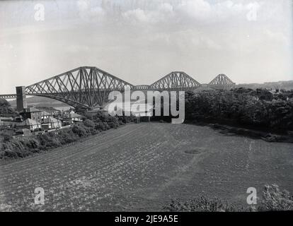 1956, vue historique de cette époque du Forth Bridge, la première grande structure d'acier au monde. Un pont ferroviaire en porte-à-faux traversant le Firth of Forth dans l'est de l'Écosse, près d'Édimbourg, son ouverture en 1890 a été une pierre angulaire majeure dans le génie civil ferroviaire moderne et détient encore aujourd'hui le record du plus long pont en porte-à-faux au monde. Il a été conçu avec trois sections pour la force, car il y a de forts vents qui soufflent à travers la quatrième, qui avait causé en 1879 l'effondrement du premier pont de chemin de fer Tay. Banque D'Images