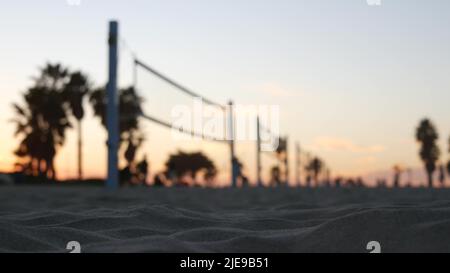 Joueurs jouant au volley-ball sur la plage, jeu de volley-ball avec balle et filet, silhouette de palmiers au coucher du soleil, côte californienne, États-Unis. Des gens défocused sur la rive sablonneuse de l'océan. Cinémagraphe sans couture. Banque D'Images