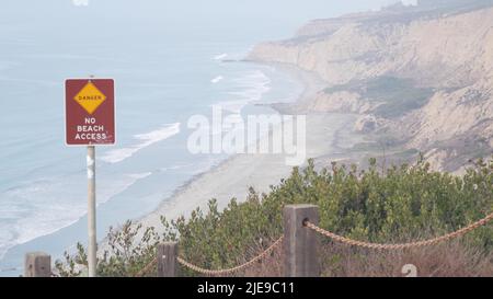 Falaise instable abrupte, roche ou bluff, temps brumeux, érosion de la côte de Californie, États-Unis. Le crag érodé de Torrey Pines donne sur le point de vue, les vagues de l'océan d'en haut. Garde-corps de chaîne pour trekking de sécurité, signe de danger. Banque D'Images