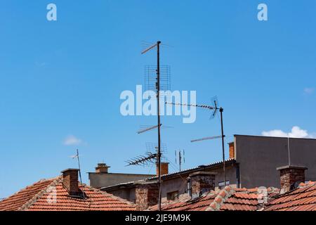 De nombreuses antennes TV analogiques sur le toit rouge des maisons et le ciel bleu en arrière-plan, un jour d'été. Le style rétro du signal de télévision. Copier l'espace Banque D'Images