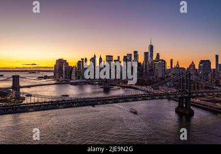 De grands ponts câblés enjambant East River. Horizon avec gratte-ciel du centre-ville et ciel romantique et coloré au coucher du soleil. Manhattan, New York, États-Unis Banque D'Images