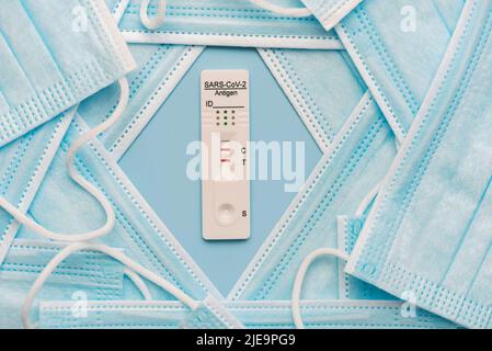 Vue de dessus des masques chirurgicaux de protection et du kit de test rapide positif de l'antigène pour COVID-19 sur fond bleu Banque D'Images