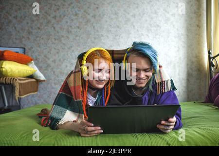 Portrait d'un jeune couple punk tatoué d'une fille et d'un gars avec de longs cheveux teints tressés, allongé sur un grand lit vert. Ils écoutent de la musique. lar jaune Banque D'Images