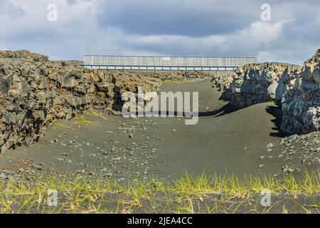 Paysage au soleil sur la péninsule de Reykjanes en Islande. Pont métallique sur deux falaises. Sable noir de lave avec herbe sur les fissures de l'Eurasie et du Nord Banque D'Images