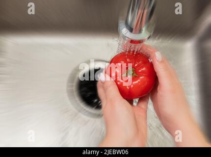 les mains des femmes lavant une tomate dans la cuisine avec effet de flou de mouvement Banque D'Images