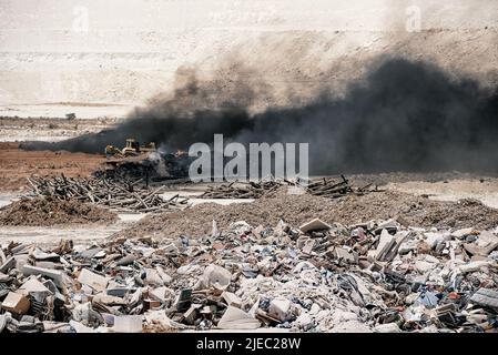 Tirer à la décharge. Fumée noire provenant de la combustion de vieux pneus et de la lutte contre le feu avec le bulldozer Banque D'Images