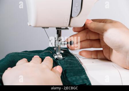 Femme de créateur ou tailleur travaillant sur machine à coudre. Les mains tiennent et coudre les détails des vêtements. Le monde s'adapte à tous les jours. Gros plan du processus de couture. Banque D'Images