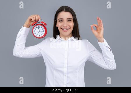 Fille tenant un réveil montre. Portrait d'une jeune femme drôle et belle avec un réveil debout sur fond gris. Banque D'Images