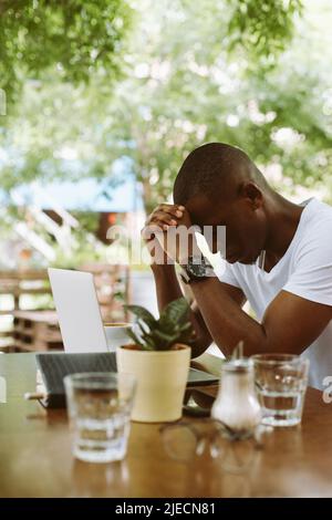 Vertical stressé peau sombre homme pendu sa tête sur les mains des articulations près de l'ordinateur portable dans le café. Maux de tête et migraine parce que le travail Banque D'Images