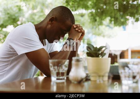 Épuisé, stressé peau sombre homme se penchait la tête sur les mains des articulations près de l'ordinateur portable et du smartphone. Conférence en ligne dans le café Banque D'Images