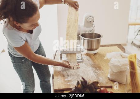 Une femme est engagée dans la cuisson des nouilles. Table avec sac de farine pour mélangeur de pâte et coupe-nouilles Banque D'Images