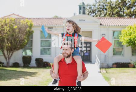 Le père soutient et motive son fils. Un enfant enthousiaste qui va à l'école primaire. Papa et son fils ont été surpris de s'amuser près de la cour de l'école. Concept de famille amicale. Banque D'Images