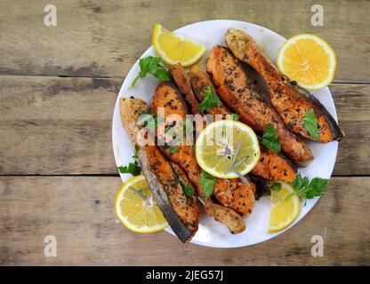 Saumon rôti au four avec beurre, persil et ail. Portion de poisson cuit et citron frais sur une assiette blanche sur le fond en bois, vie supérieure Banque D'Images