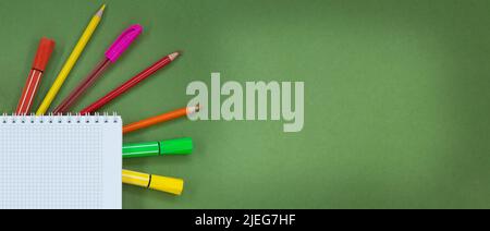 Stylos multicolores, crayons, stylos feutres avec bloc-notes avec cellule sur fond vert. Concept de retour à l'école, l'apprentissage, le dessin. Copier l'espace Banque D'Images