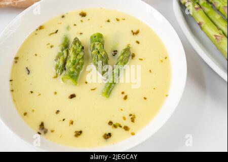 Soupe aux asperges dans une assiette blanche, partie de l'assiette avec asperges sur fond blanc, gros plan. Banque D'Images