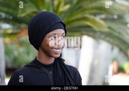 Jeune femme africaine vêtue tout en noir d'un sourire gagnant et d'un regard doux Banque D'Images