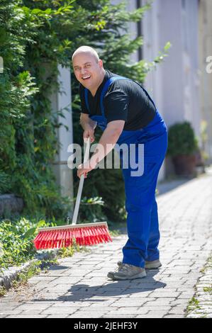Kehrwoche, Mann reinigt eine Strasse mit dem Besen, Banque D'Images