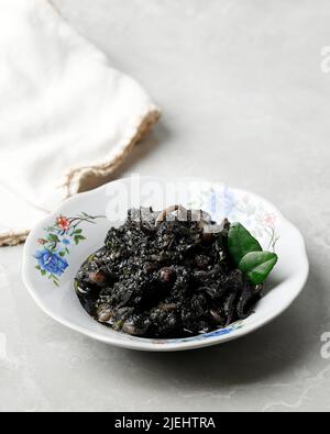 Remuez le courge et le Chili frits dans la sauce à l'encre noire du calamar servie dans une assiette en céramique. Connu sous le nom de Tumi Cumi Hitam Pedas en Indonésie. Banque D'Images