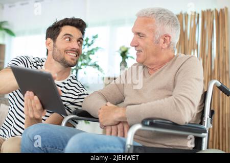 homme à la retraite gai et handicapé assis en fauteuil roulant près de son fils barbu Banque D'Images