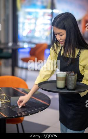 Femme mettant des montagnes russes sur une table au café Banque D'Images