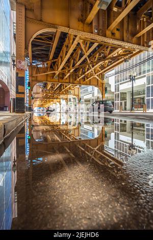 « Sous l'El » Chicago, lignes de chemin de fer aériennes à la salle/gare Van Buren. Les voitures passent et les pistes se reflètent dans une flaque. Chicago, Illinois, États-Unis Banque D'Images