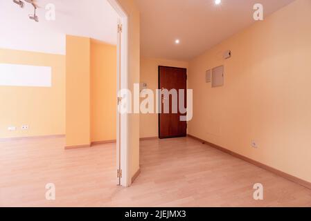 Hall d'entrée d'une maison avec une porte en bois, parquet en chêne et murs peints jaune clair avec accès à une plus grande pièce Banque D'Images